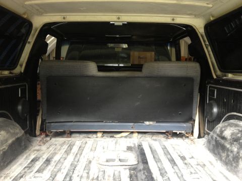 1979 Ford Bronco - The cargo area of a light-colored SUV shows a folded rear seat and a FedEx box, suggesting a model year around 1978.