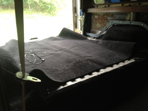 1979 Ford Bronco - The interior of a vehicle is shown with new black carpet being laid down. A metal latch is visible on the left side.