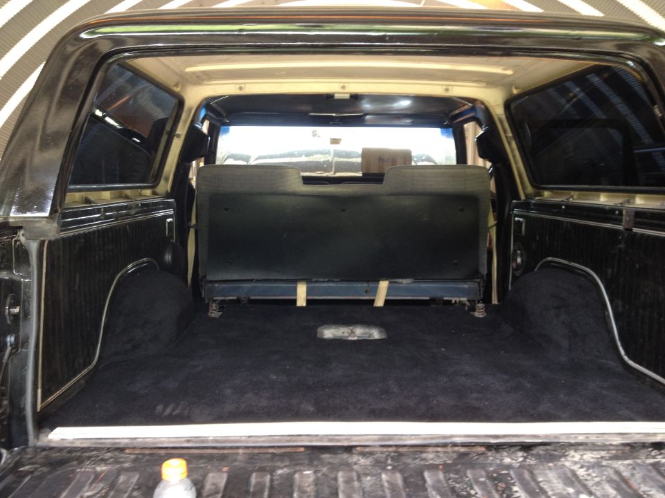 Interior cargo area of a 1979 Ford Bronco, black carpet, folded rear seat