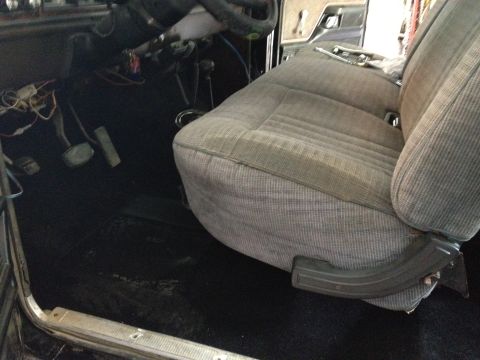 1979 Ford Bronco - The interior of a vehicle is shown, a grey fabric seat and black carpeting on the floor.