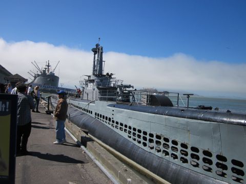 1991 Ford LTD Crown Victoria - A submarine is docked at a pier on a sunny day, with another ship visible in the distance.