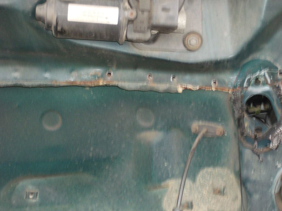Green car firewall with motor and rusted edge. Holes drilled along the top edge