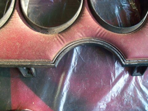 1979 Ford Ranchero - Extreme close-up of a removed instrument cluster bezel with a red grained-vinyl face and dark-painted trim rings around the round gauge ope…