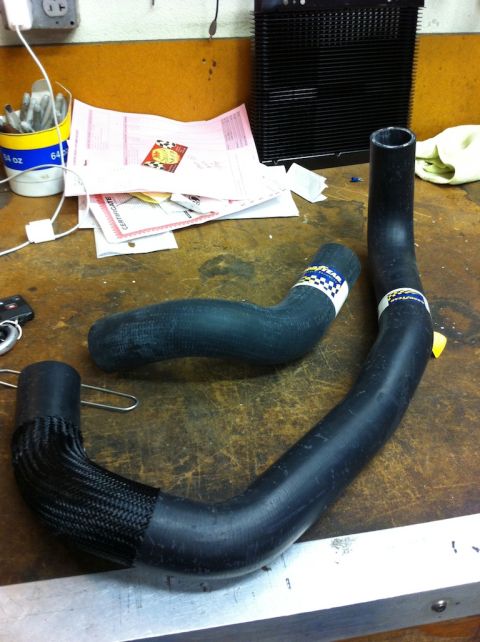2010 Dodge Challenger - Two radiator hoses are laid out on a workbench with various papers and a black cooling finned component in the background.