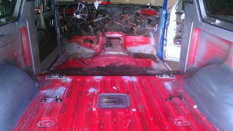 1978 Ford Bronco - The interior of a vehicle is shown with its dashboard disassembled and the floor stripped to red primer, indicating a restoration project.