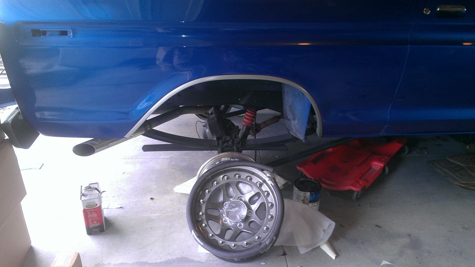 blue pickup truck rear axle with suspension and exhaust pipe, a wheel is off and on the ground