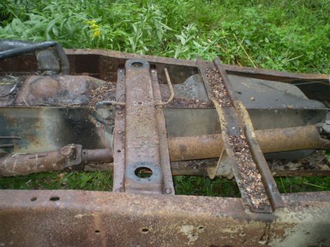 1979 Ford Bronco - Close-up of a heavily rusted vehicle frame, including the fuel tank and driveshaft, in an outdoor setting.