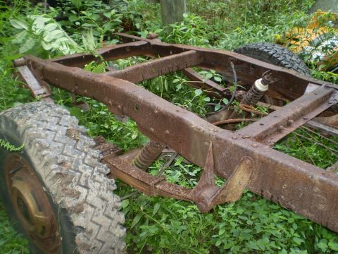 1979 Ford Bronco - The heavily rusted frame and suspension components of an old vehicle sit in overgrown grass.