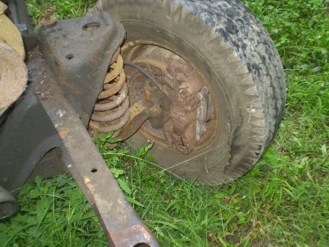 1979 Ford Bronco - Close-up of a rusty vehicle suspension part and tire resting on grass.