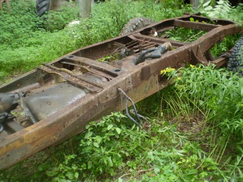 1979 Ford Bronco - A heavily rusted vehicle frame sits abandoned in overgrown vegetation, showing signs of decay and disuse.