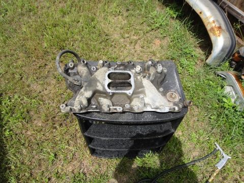 1994 Ford Bronco - An intake manifold, likely from a Ford vehicle, sits on the grass next to other car parts.