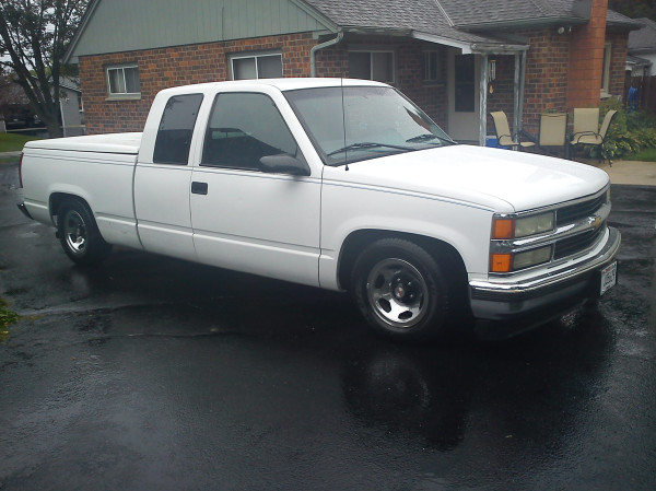 White Chevy extended-cab pickup with lowered stance on wet driveway in the rain