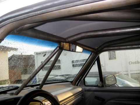 1996 Ford Bronco - Custom roll cage installed inside a vehicle, with a trailer visible through the rain-streaked windows.