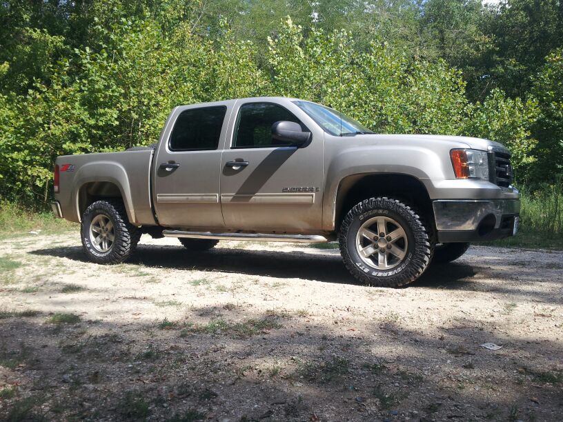 Silver GMC Sierra pickup truck parked on a dirt road with trees in the background