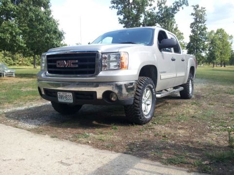 1995 Ford F-150 - A silver GMC Sierra pickup truck is shown from a three-quarter front angle on a dirt and grass surface.