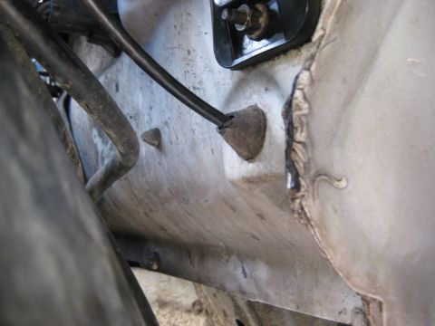 1994 Ford Bronco - A close-up view of a rubber grommet and wiring harness on the underside of a vehicle.