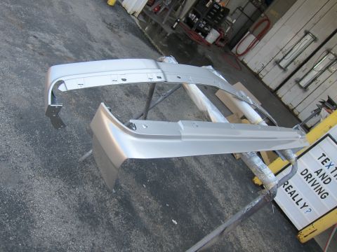 1991 Ford LTD Crown Victoria - Two silver car bumpers are displayed on stands in an outdoor setting, with a sign in the background.