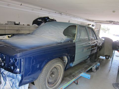 1991 Ford LTD Crown Victoria - A blue sedan is in a garage, partially covered and undergoing bodywork and painting.