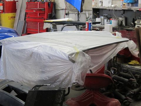 1991 Ford LTD Crown Victoria - A car hood covered in plastic sheeting sits in a workshop, obscuring its details.