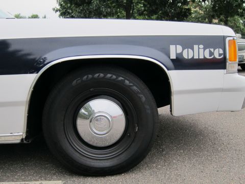1991 Ford LTD Crown Victoria - Close-up side view of a 1991 Ford Crown Victoria police car, showing the fender, wheel, and 'Police' lettering.