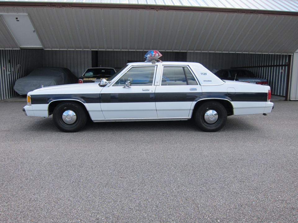 Side view of a white and black police car with a light bar on top. It has the number 1139 on the rear door