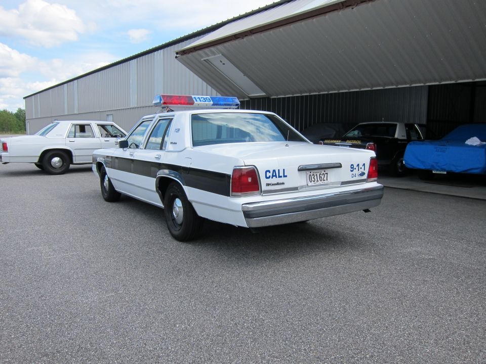 White police car with light bar, rear view. License plate 031627