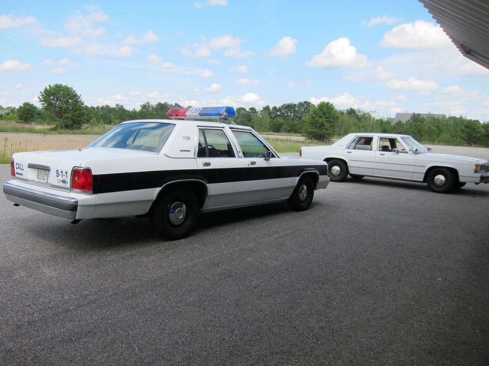 White and black police car, rear view, with light bar. Another white car is parked behind it