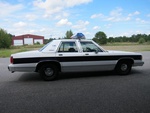 1991 Ford LTD Crown Victoria - This 1991 Ford Crown Victoria LTD police car is seen from the side with a black stripe and a light bar on the roof.
