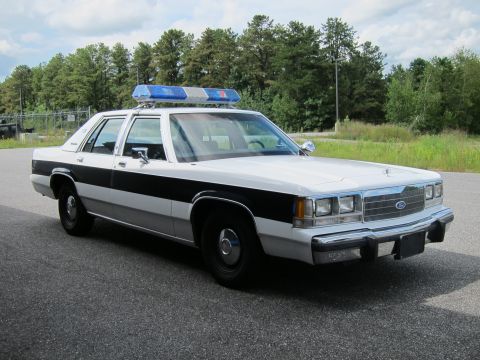 1991 Ford LTD Crown Victoria - This 1991 Ford Crown Victoria LTD police car is parked on asphalt with trees in the background.