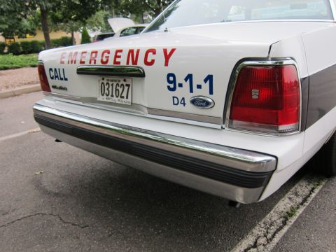 1991 Ford LTD Crown Victoria - Rear view of a 1991 Ford Crown Victoria LTD police car, displaying 'EMERGENCY CALL 9-1-1' and a license plate.
