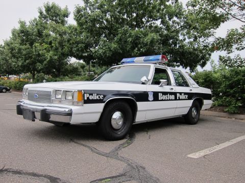 1991 Ford LTD Crown Victoria - A white 1991 Ford Crown Victoria LTD police car is parked outside with trees in the background.