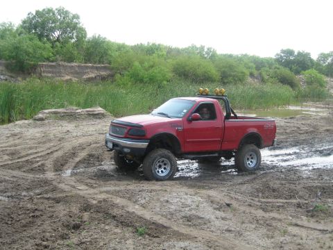 1990 Ford Bronco - This lifted red Ford F-150 is navigating a muddy off-road course.