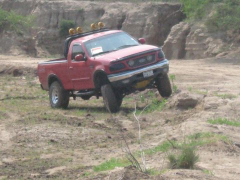 1990 Ford Bronco - This red pickup truck is navigating a steep dirt incline, its off-road capabilities.