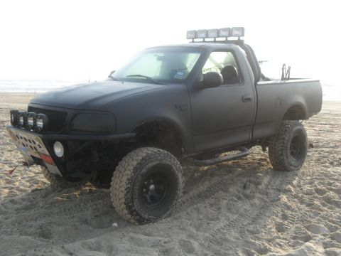 1990 Ford Bronco - This modified pickup truck is parked on a beach, suggesting off-road capabilities.