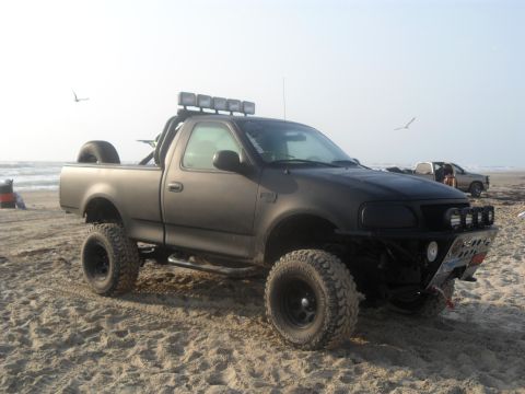 1990 Ford Bronco - Custom pickup truck with off-road modifications parked on the beach near the ocean.