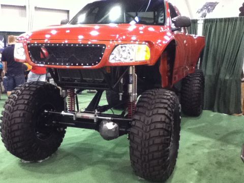 1990 Ford Bronco - A heavily modified red truck with large off-road tires is on display.