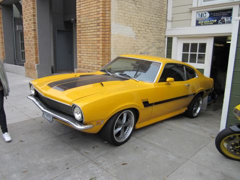 1991 Ford LTD Crown Victoria - Yellow 1970 Ford Maverick coupe parked outside a building with black racing stripes.