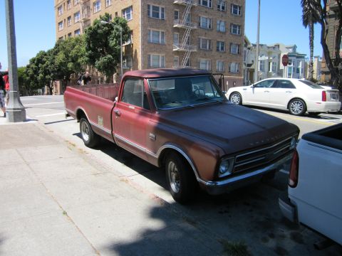 1991 Ford LTD Crown Victoria - A vintage Chevrolet pickup truck is parked curbside on a sunny day in front of an apartment building.