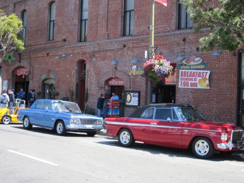 1991 Ford LTD Crown Victoria - Two classic cars, a red convertible and a blue sedan, are parked on a street in front of a brick building.