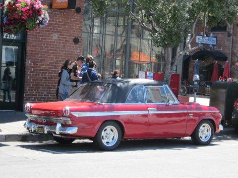 1991 Ford LTD Crown Victoria - A classic red convertible with a black top is parked on a city street, with people gathered nearby.