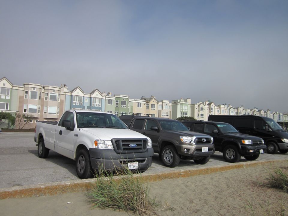 White Ford F-150 pickup truck parked on a sandy lot, front 3/4 view