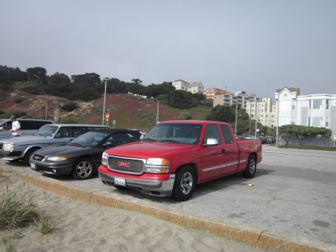 1991 Ford LTD Crown Victoria - A red GMC pickup truck is parked in a lot near the coast, with other vehicles visible.