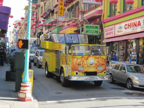 1991 Ford LTD Crown Victoria - A bright yellow fire truck with flame graphics drives down a street lined with shops and red lanterns.