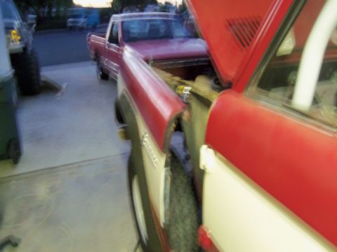 1968 Ford Bronco - A red and white pickup truck is parked next to another vehicle, which has its hood open, revealing the engine compartment.