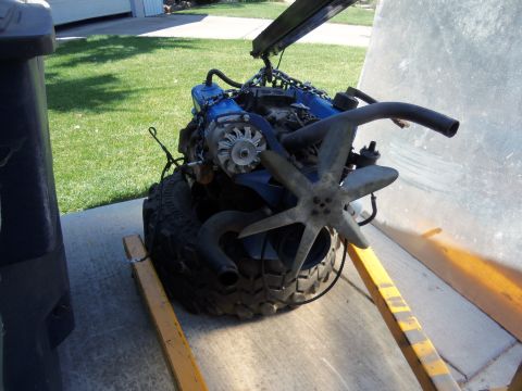 1968 Ford Bronco - An engine is suspended by chains and resting on a tire, supported by an engine stand outdoors.