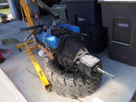 1968 Ford Bronco - Engine and transmission assembly resting on a large tire, with a yellow engine hoist attached.