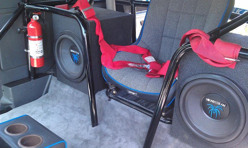 Bronco interior with roll cage, two Soundstream subwoofers, red racing harness, and mounted fire extinguisher