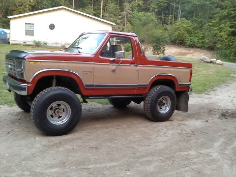1984 Ford Bronco - This lifted Ford Bronco has a two-tone paint scheme and is parked on a dirt road.