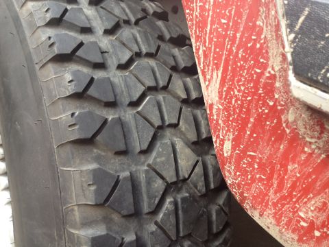 1984 Ford Bronco - A close-up view shows the tread pattern of an off-road tire and a mud-splattered red vehicle fender.