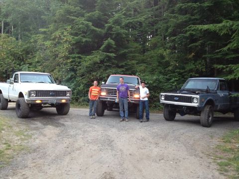 1984 Ford Bronco - Three pickup trucks and three people pose for a photo on a dirt road in a wooded area.